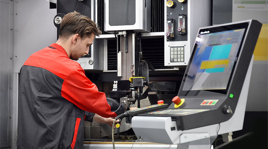 Das Bild zeigt einen Werkzeugbautechniker von weba Olomouc, der konzentriert eine moderne Erodiermaschine bedient. Seine Hände sind geschickt damit beschäftigt, die Maschine zu steuern.