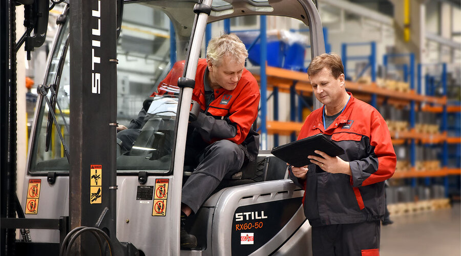 Zwei Werkzeugbautechniker besprechen die Logistik in der Serienproduktion. Einer sitzt im Stapler und betrachtet das Tablet, das der andere Werkzeugbautechniker in der Hand hält.