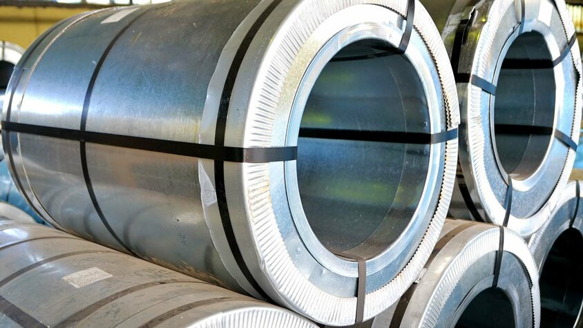 weba Werkzeugbau - Warmumformung Materialien Mehrere übereinander gestapelte Stahlblechrollen in einer Halle, die mit schwarzen Umreifungsbändern gesichert sind. Das Bild wird symbolisch im Blog Warmumformung Materialien verwendet.