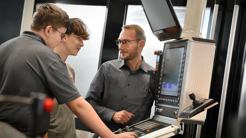 Lehre in Steyr - Lehrstelle Zerspanungstechnik Ein Lehrlingsausbilder erklärt zwei Lehrlingen im Bereich Metalltechnik, Modul H8 Zerspanungstechnik, die Steuerung eines Bearbeitungszentrums. Die Lehre in Steyr bei weba kombiniert praktische Erfahrung mit theoretischen Know-how in der Zerspanungstechnik.