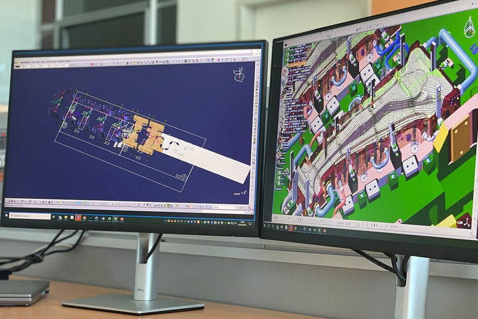 Zwei PC-Bildschirme, einer zeigt ein detailliertes Close-up einer CAD Konstruktion eines Warmumformwerkzeuges zur Produktion von B-Säulen, während der andere Bildschirm den Transferaufbau eines Werkzeuges darstellt.