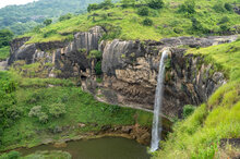 Ein beeindruckender Wasserfall stürzt von einer steilen Klippe in ein ruhiges Becken, umgeben von üppigem Grün und felsigen Formationen.