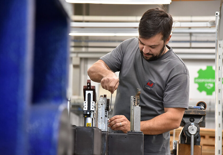 Kovový technik ve společnosti weba Werkzeugbau v akci, zaměřený na montáž měřicích přípravků ve výrobní hale. Technik, oblečený v čistém a praktickém pracovním oděvu, pracuje precizně u dobře osvětleného pracovního stolu. Obklopen různými nástroji a součástkami ukazuje snímek detaily a přesnost, které jsou při výrobě nářadí vyžadovány. Scéna navozuje pocit odbornosti a nasazení ve výrobním procesu, což je charakteristické pro vysoké standardy kvality společnosti weba. Obrázek symbolizuje pracovní místa v Olomouci pro zkušené a profesionální pracovníky společnosti weba.
