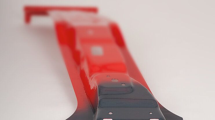 Eine B-Säule, gefertigt aus höchstfestem Material, präsentiert sich in einem leuchtenden Rot. Besonders hervorgehoben ist eine Softzone, die für maßgeschneiderte Crasheigenschaften entwickelt wurde; diese Zone hebt sich in einem tiefen Anthrazitgrau deutlich vom restlichen Teil der Säule ab. Die Kontrastierung der Farben betont die speziellen Eigenschaften der B-Säule und die technische Innovation, die hinter der Entwicklung maßgeschneiderter Sicherheitsmerkmale steht. 