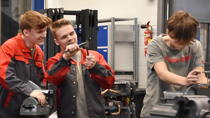 Lehrstelle Steyr - Lehre bei weba Werkzeugbau Foto von Lehrlingen in einer Lehrwerkstätte in ihrer Lehrstelle in Steyr bei der Arbeit: Zwei Lehrlinge unterhalten sich über eine technische Zeichnung, zwei weitere messen ein Stahlstück und ein Lehrling arbeitet an einem Spannbock.