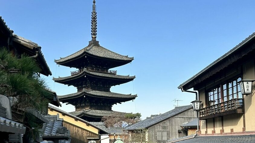 Die Pagode von Kyoto Eine traditionelle japanische Straße mit Holzhäusern und einer beeindruckenden Pagode im Hintergrund unter blauem Himmel.
