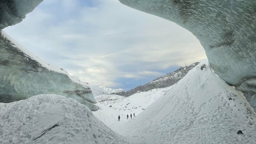 Gletscherblick in Alaska Blick aus einer Gletscherhöhle auf eine verschneite Landschaft mit fernen Bergen. Drei Personen sind in der Ferne sichtbar.