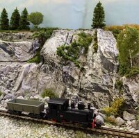 Black model steam locomotive with freight wagons set against a detailed rocky landscape.