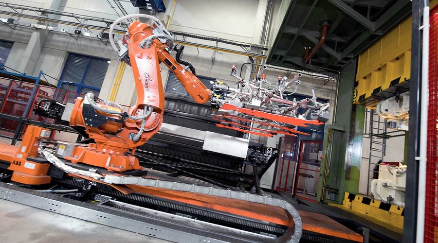 Roboterarme transferieren vier glühende Platinen von einem Kammerofen in ein Werkzeug für das Presshärten