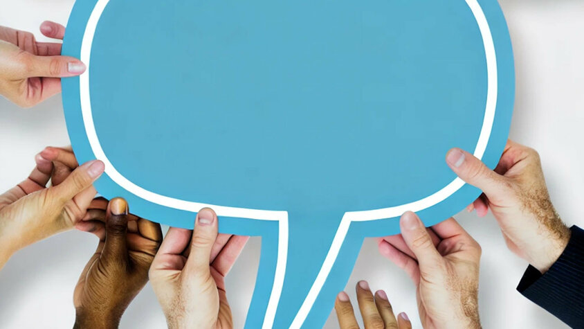 Jobs in Steyr - Karriereratgeber Eine Gruppe von verschiedenen Händen, die gemeinsam eine große blaue Sprechblase halten. Die Sprechblase ist leer und symbolisiert Kommunikation und Zusammenarbeit. Der Hintergrund ist schlicht, was die gemeinschaftliche Anstrengung zur Unterstützung der Sprechblase hervorhebt.