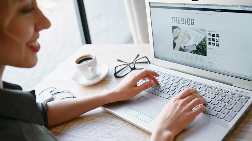 weba Werkzeugbau Blog - Innovationen in der Warmumformung Foto einer Frau, die konzentriert an einem Laptop arbeitet. Auf dem Bildschirm des Laptops ist deutlich "The Blog" zu sehen, was darauf hindeutet, dass sie entweder an einem Blogbeitrag schreibt oder Bloginhalte durchstöbert.