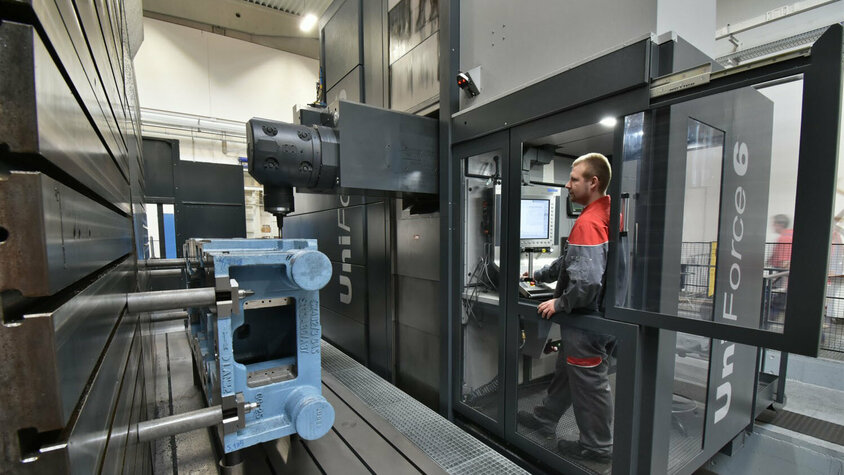 weba Werkzeugbau - Hochmodernes Bearbeitungszentrum für höchste Präzision in der Zerspanung Eine SHW-Maschine beim Bearbeiten eines Gussteils. Die Bedienerkabine und die Winkelaufspannung mit dem aufgespannten Gussteil sind deutlich zu sehen. Die Maschine arbeitet präzise, während der Bediener die Prozesse überwacht. I