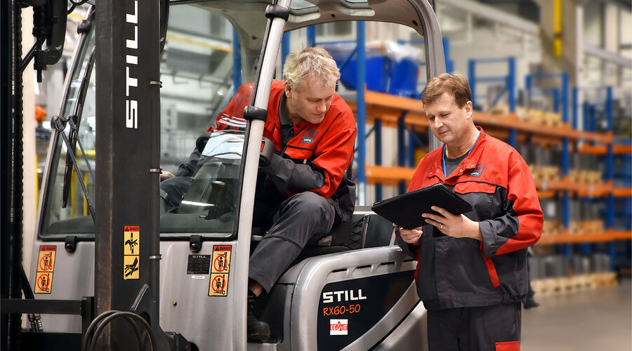 Zwei Werkzeugbautechniker besprechen die Logistik in der Serienproduktion für das Presshärten. Einer sitzt im Stapler und betrachtet das Tablet, das der andere Werkzeugbautechniker in der Hand hält.