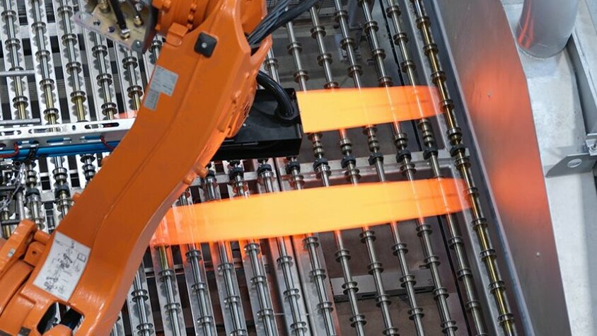 Prozesstechnik für das Presshärten bei weba Werkzeugbau Industrieller Roboterarm in der Prozesstechnik für das Presshärten positioniert glühend heiße Metallbleche auf einer Produktionsanlage. Der Einsatz modernster Technologie optimiert den Presshärteprozess und gewährleistet eine präzise Steuerung der Umformprozesse bei weba Werkzeugbau.