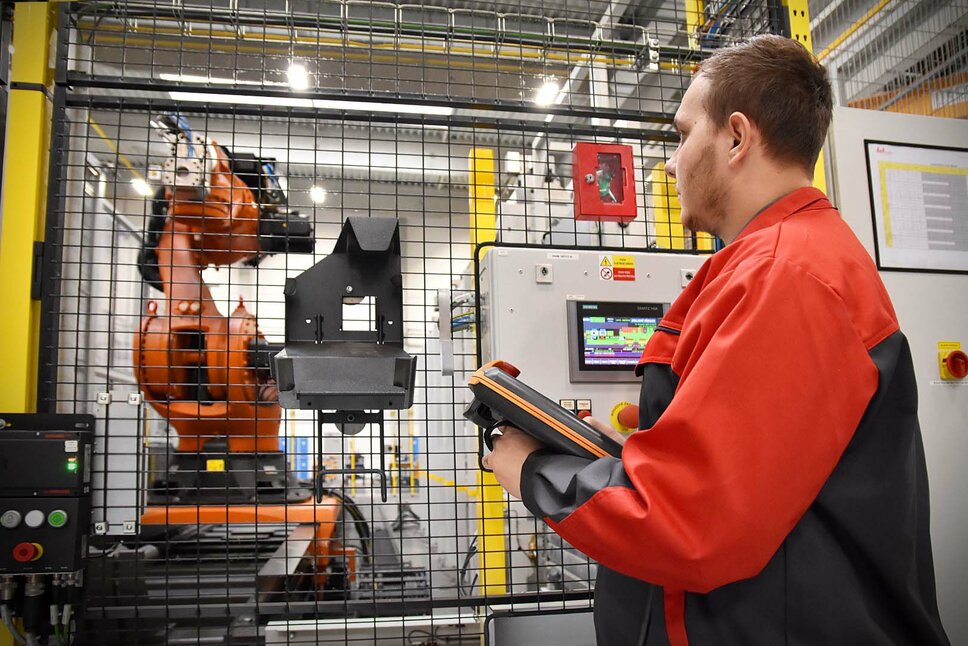 Obráběcí technik programuje automatizovanou obráběcí linku ve společnosti weba Olomouc. Soustředí se na přenosový chapadlo a v rukou drží ovládací tablet.