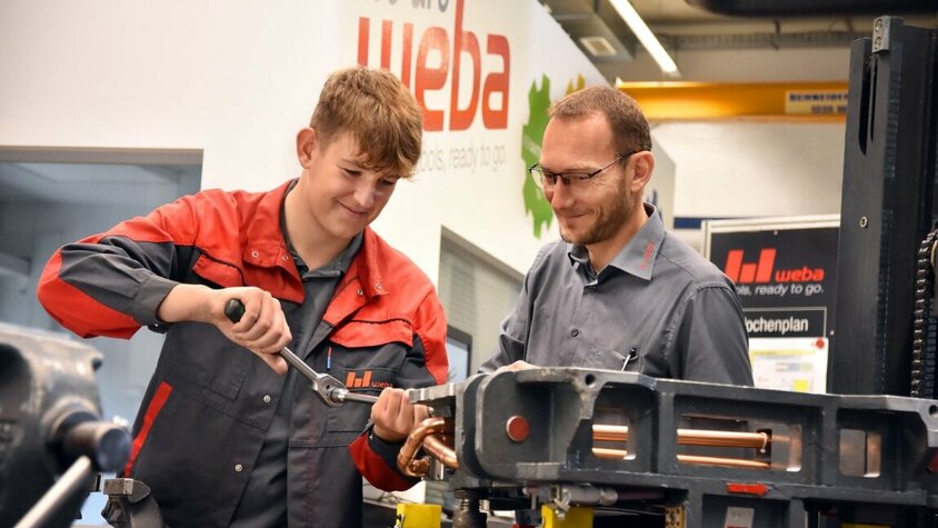 Lehre in Steyr - Ausbildung als Werkzeugbautechniker bei weba Werkzeugbau Ein Lehrling in der Werkzeugbautechnik arbeitet an einer Miniatur eines Umformwerkzeugs, während der Ausbilder aufmerksam zuschaut. weba Werkzeugbau bietet Lehre in Steyr in der Metalltechnik an.