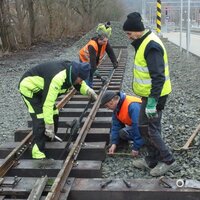 Several members of a model railway club work together on tracks outdoors.