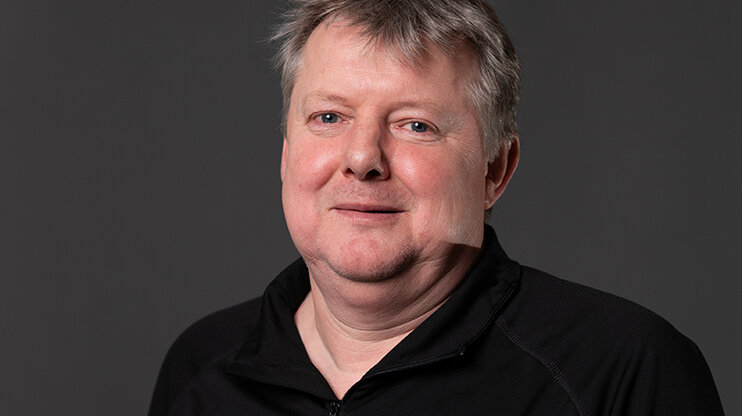 Klaus Postlbauer, Process Manager in Toolmaking at weba, smiles at the camera against a neutral background. With a calm presence and a gentle smile, he looks directly into the lens. The image conveys competence and down-to-earth character – a perfect match for his long-standing connection with weba Werkzeugbau.