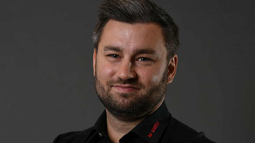 weba Werkzeugbau Kubka Alexander präsentiert sich freundlich und professionell: schwarzes Hemd mit rotem weba-Logo, vor grauem Hintergrund, direkt in die Kamera lächelnd.