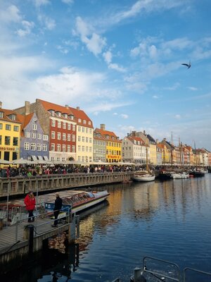 Nyhavn in Kopenhagen mit bunten Häusern, Booten im Wasser und vielen Menschen entlang der Promenade bei blauem Himmel.