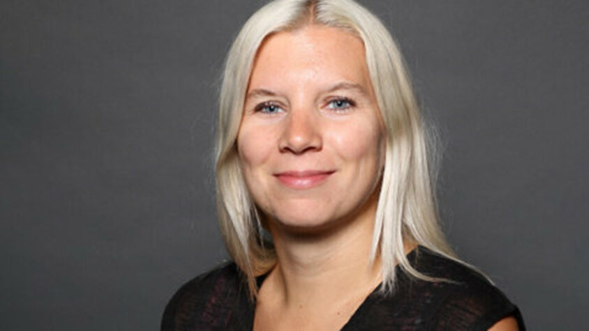 Porträtfoto von Bettina Gmainer Porträt von Bettina Gmainer, einer engagierten Mitarbeiterin bei weba Werkzeugbau, mit blondem Haar und freundlichem Lächeln vor neutralem grauem Hintergrund.