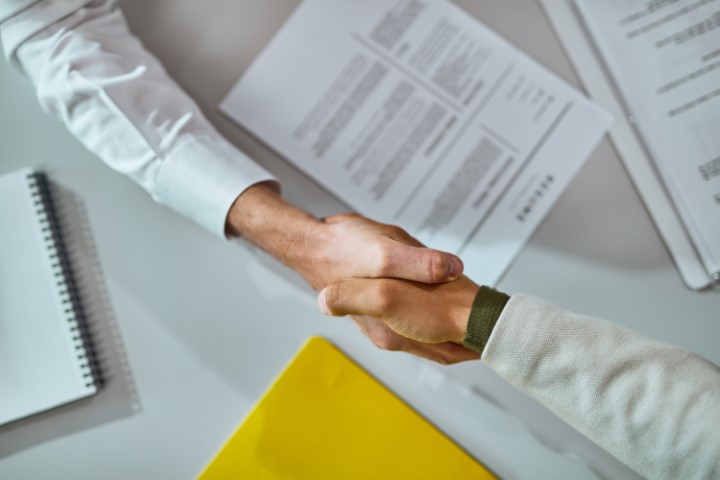 Händeschültteln nach erfolgreicher Vereinbarung über unterzeichneten Verträgen. Das Bild symbolisiert die Vertragsunterzeichnung für einen Quereinstieg.