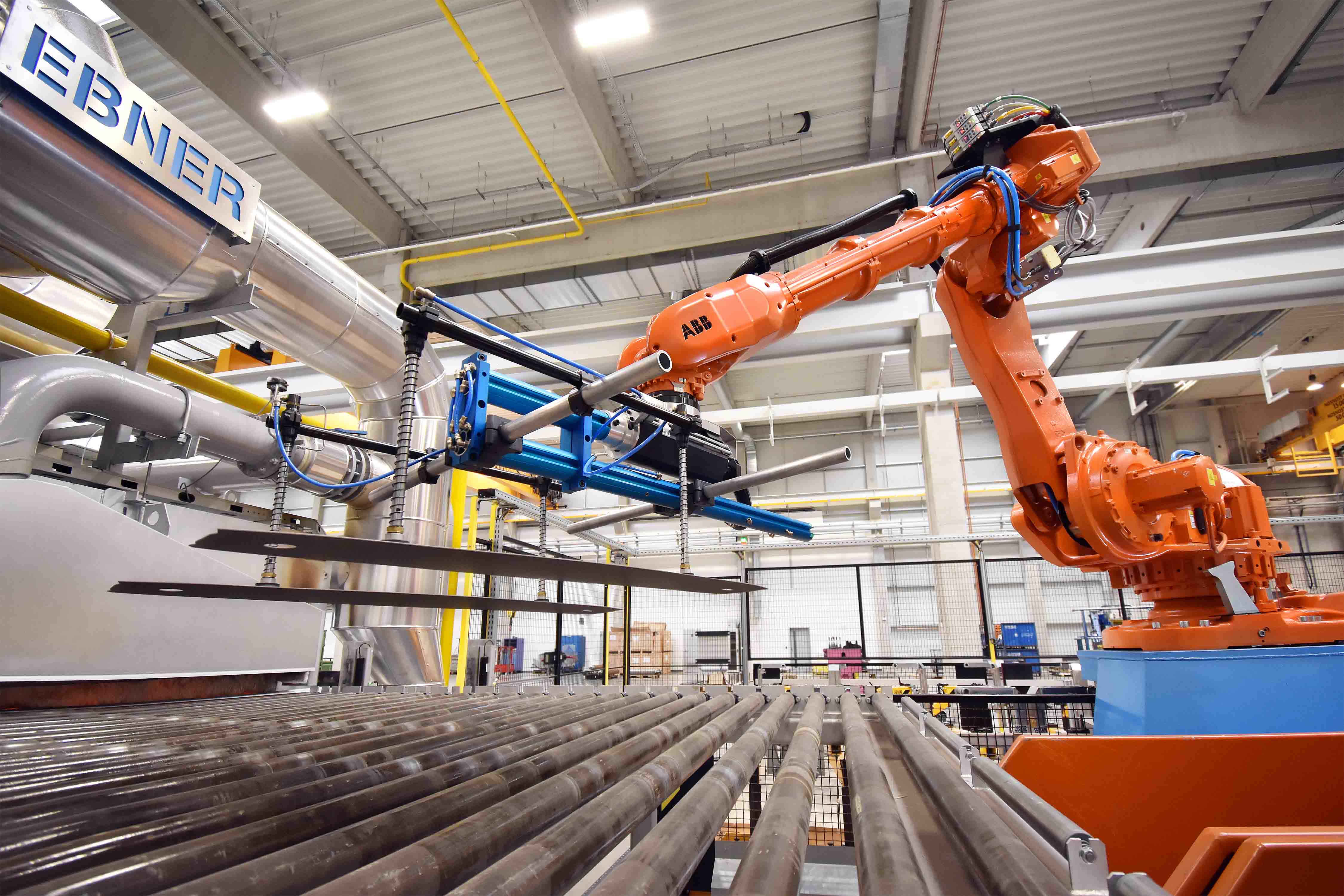 An industrial robot lifts heated sheet blanks in a modern hot forming system to prepare them for the forming process.