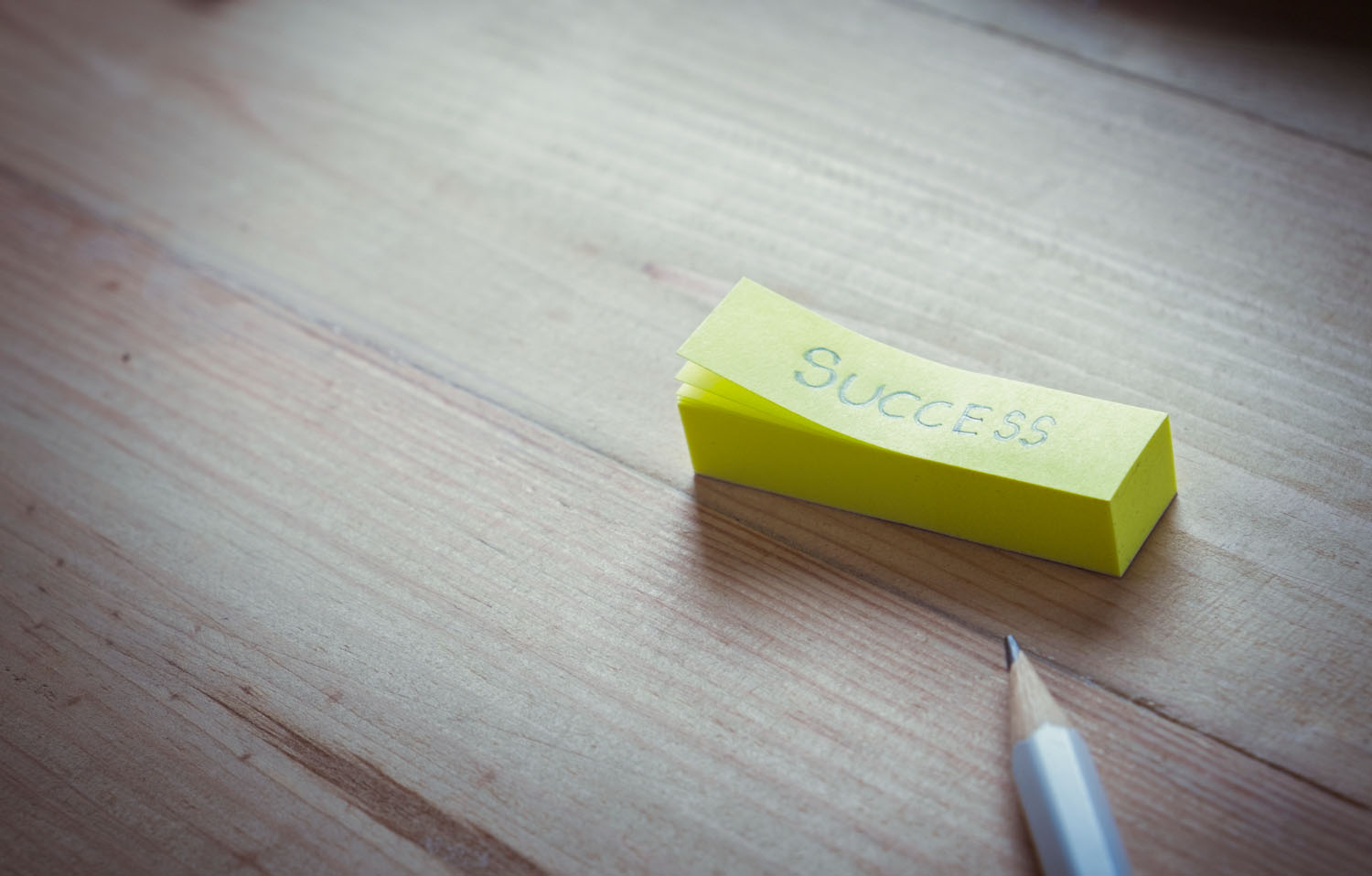 Yellow sticky note with the word "Success" on a wooden table, next to a pencil.